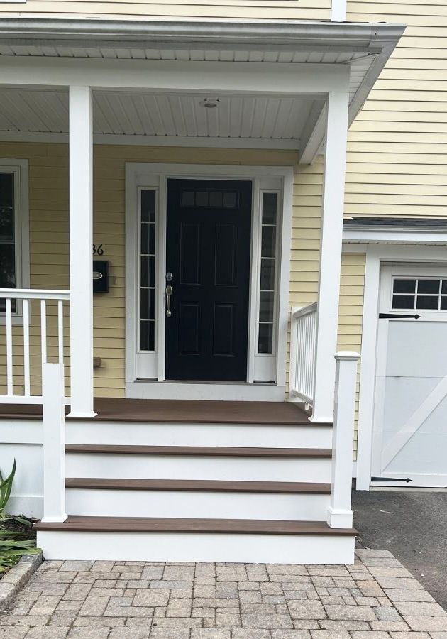 Yellow house front porch with four dark brown steps leading to a black door with sidelights and a white railing.
