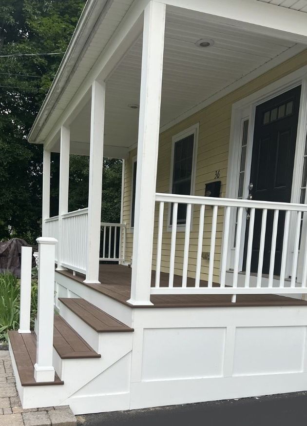 A yellow house with a porch, featuring brown steps, white railings, white support pillars, and a dark front door.