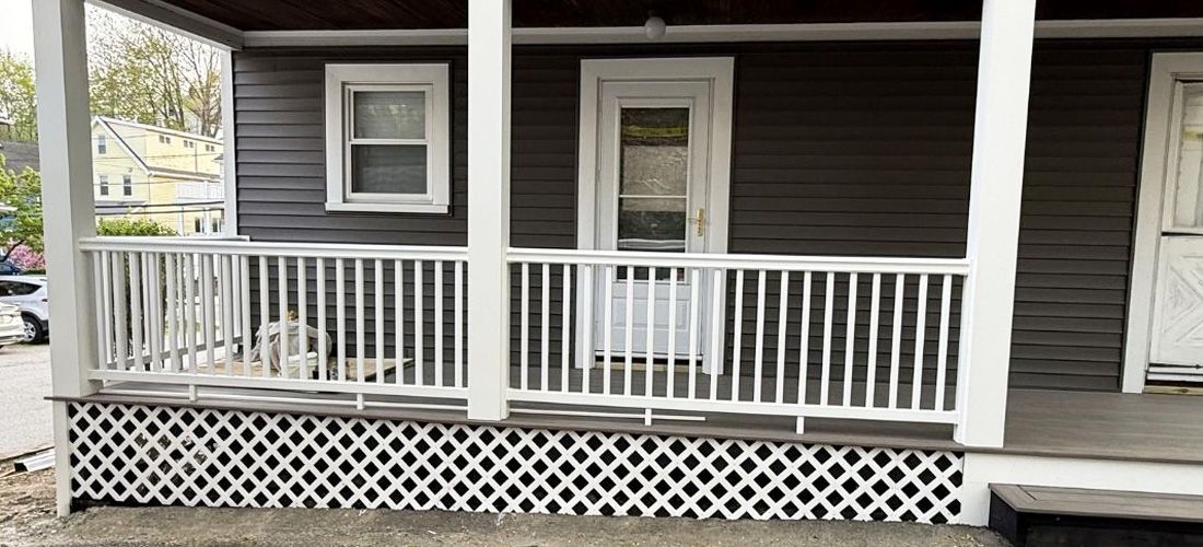 A dark grey house exterior featuring a covered porch with a white railing and white latticework underneath.