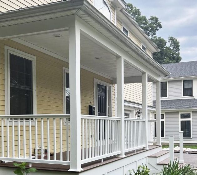 A yellow house with a covered front porch, white railings, and a black front door.