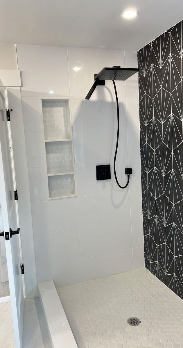 A modern shower stall with white walls, a black geometric-patterned feature wall, a built-in shelf, and a black showerhead.