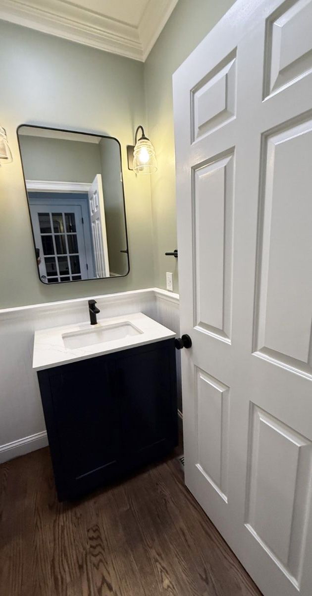 A bathroom vanity with a dark cabinet, white countertop, rectangular mirror, and sconce lighting against sage green walls.
