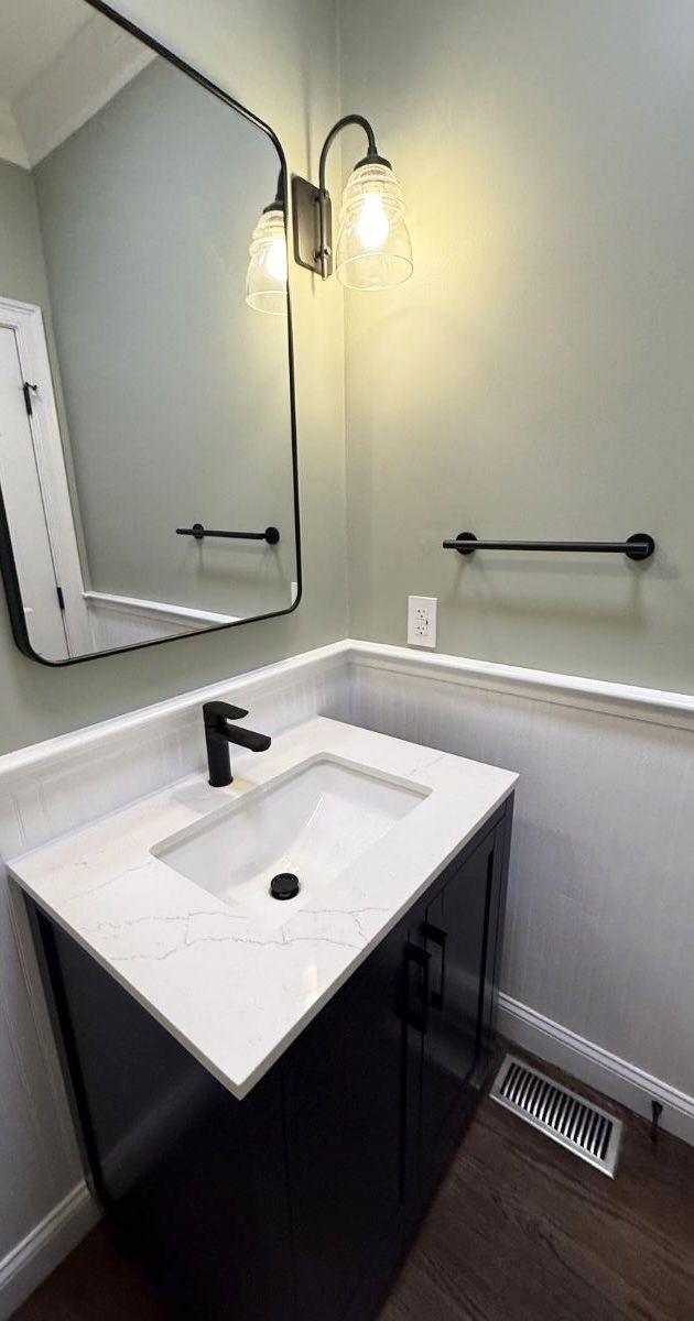 Modern bathroom vanity with dark cabinet, white marble countertop, black faucet, mirror, and wall-mounted light fixtures.