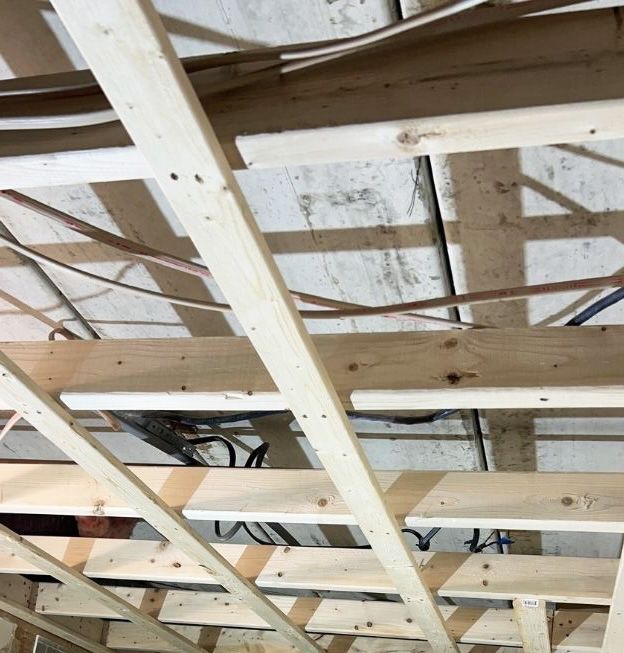 A view of exposed wooden ceiling joists and furring strips under construction, with electrical wires running throughout.