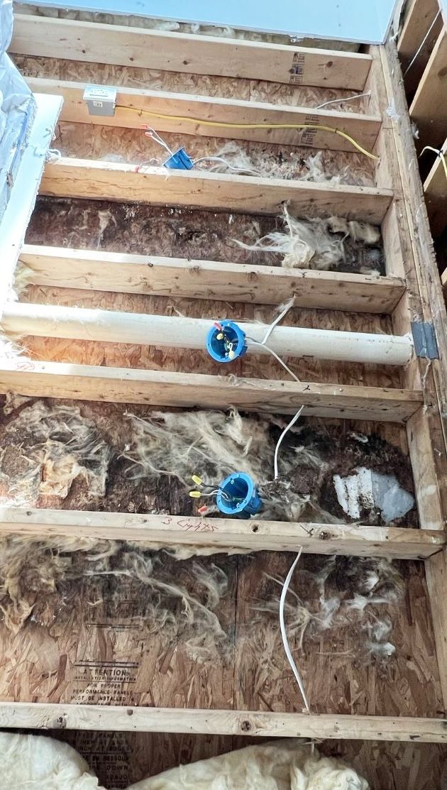 Construction framing of floor joists with blue electrical boxes and white piping installed between the wood beams.