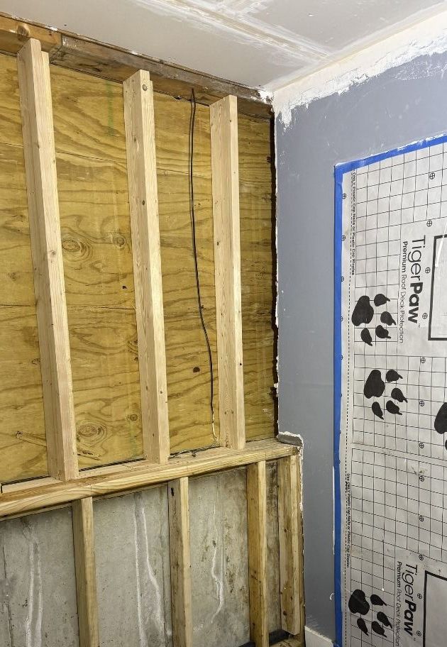 Interior wall construction showing wooden studs over plywood and a concrete foundation with a Tiger Paw floor underlay.