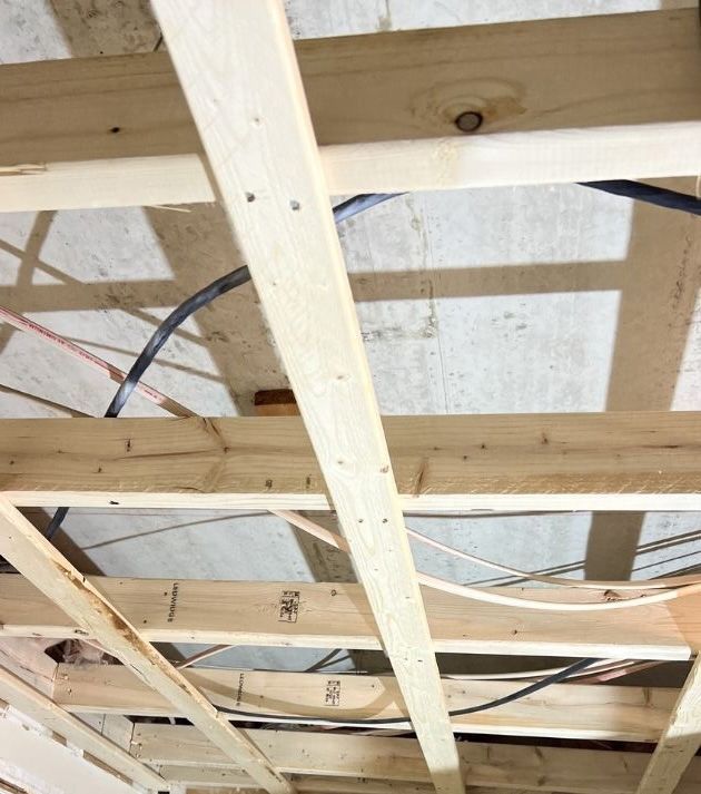 A view looking up at unfinished wooden ceiling joists and framing with electrical wiring running through them.