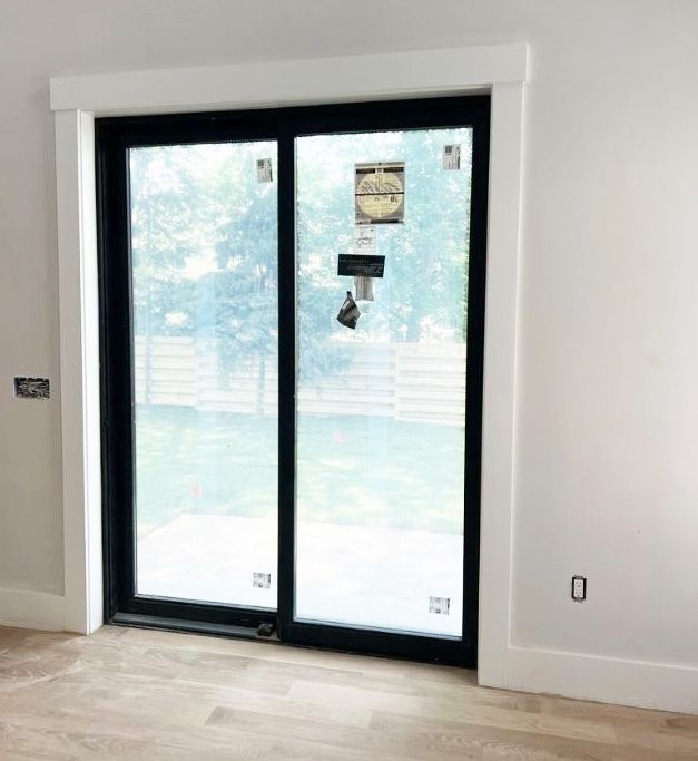 Black sliding glass patio door with white trim and baseboards in a modern, light-walled room with hardwood floors.