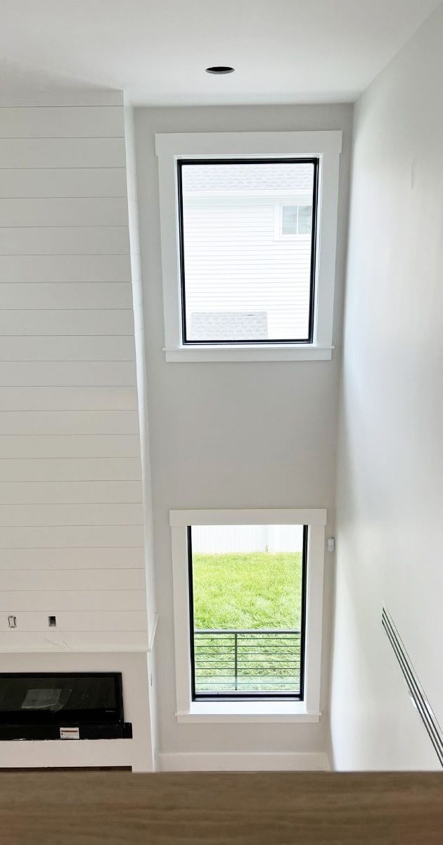 Two rectangular windows stacked vertically on a light gray wall next to a white fireplace with horizontal shiplap.