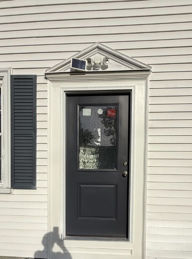 A dark door set within a white frame with an ornate triangular pediment, featuring a solar light mounted above the door.