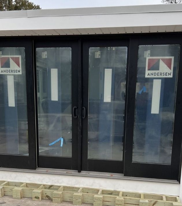 A set of four black-framed sliding glass doors by Andersen installed on a building under construction.
