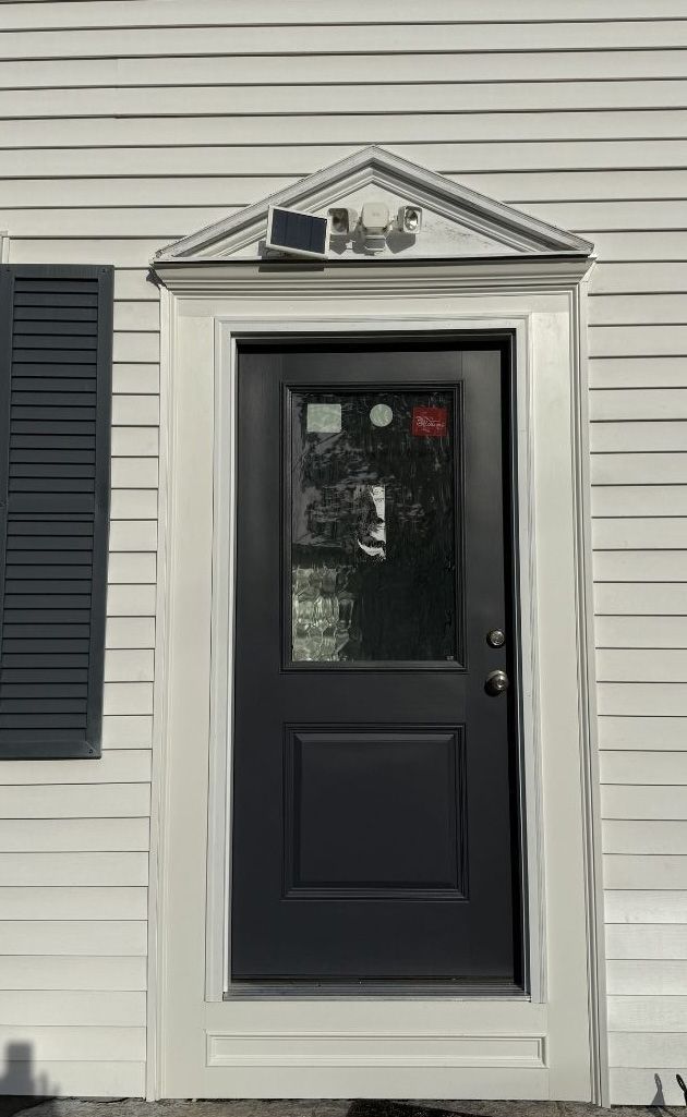 A black door with a glass pane, set in a white wall with a decorative triangular pediment above.