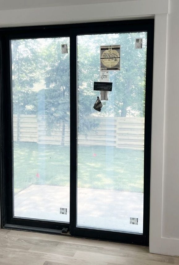 A sliding glass door with a black frame looking out onto a backyard with a wooden fence and lawn.