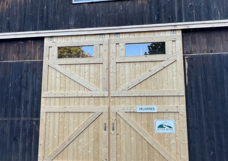 Large, light-colored wooden double barn doors with rectangular windows, set against dark wood siding.