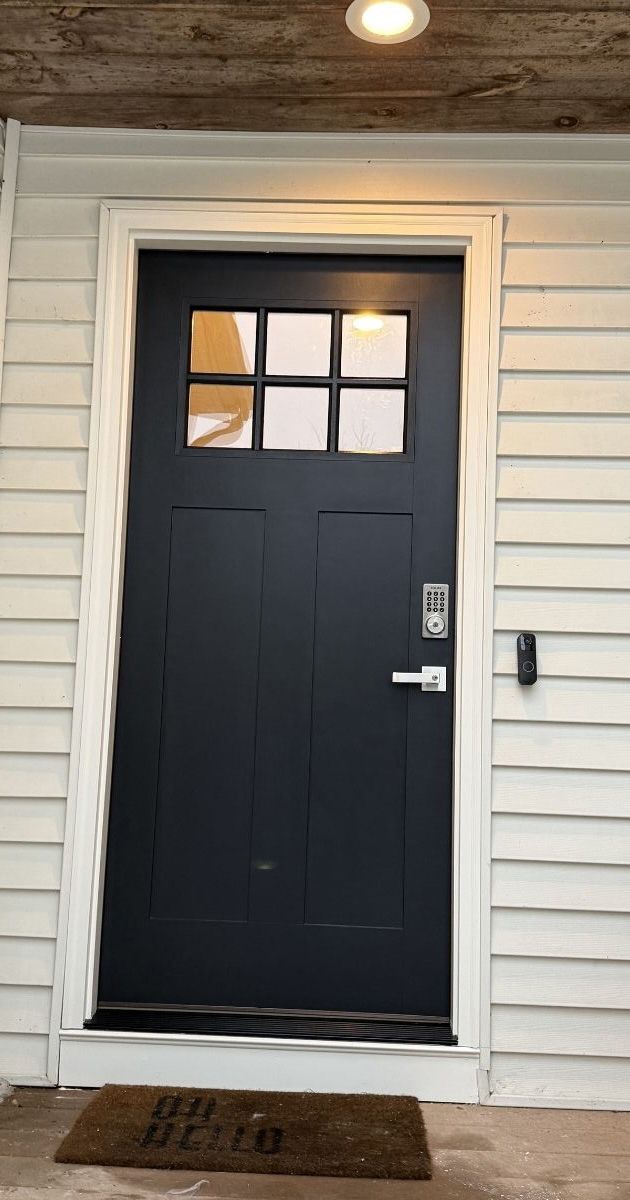 A dark blue front door with a six-pane window insert, a digital keypad lock, and a welcome mat on a porch.