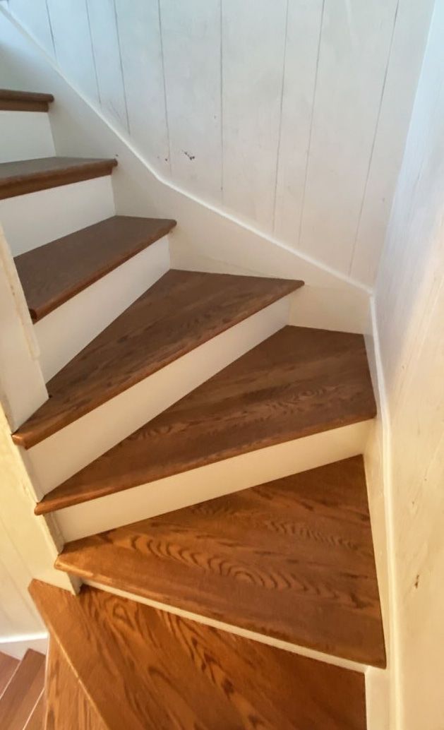 A set of wooden stairs with white risers curving upward against a white paneled wall.