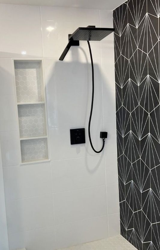 A modern shower featuring a matte black square shower head and controls against white tiles, next to a black tiled wall.