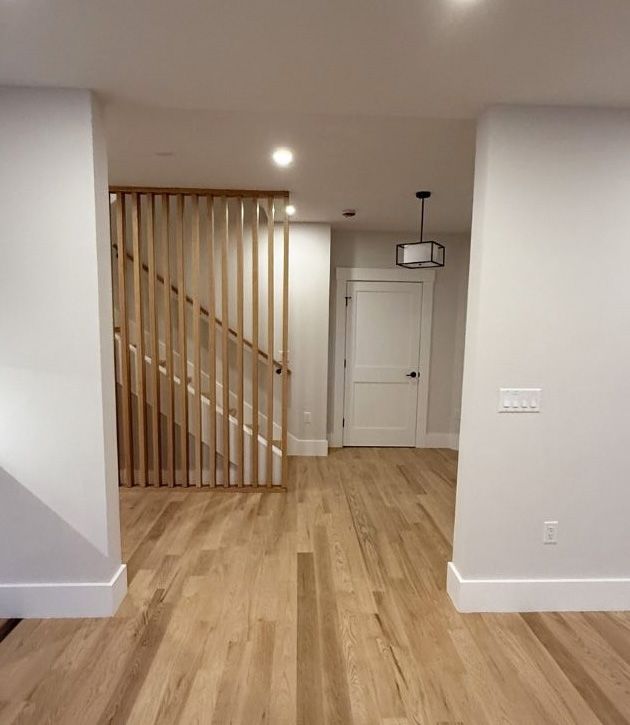 A brightly lit interior featuring light wood flooring, a wooden slatted stair railing, and a white door at the end.