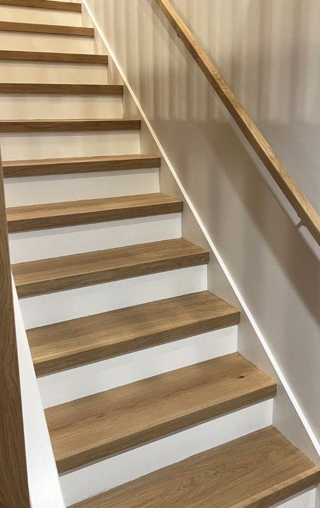 A staircase with light wood steps and white risers, featuring a matching wood handrail on the right side.