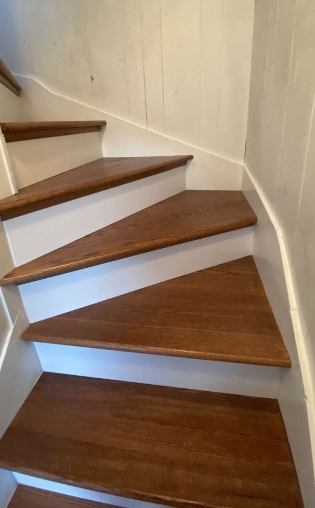 A staircase with wooden treads and white risers curves upward along a white paneled wall.