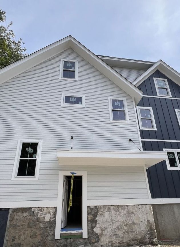 A construction site showing a two-story house exterior with light grey wavy horizontal siding and dark navy vertical siding.
