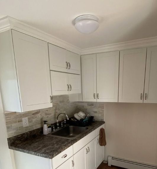 White kitchen cabinets, a stone tile backsplash, a dark countertop, and a stainless steel sink under a dome ceiling light.