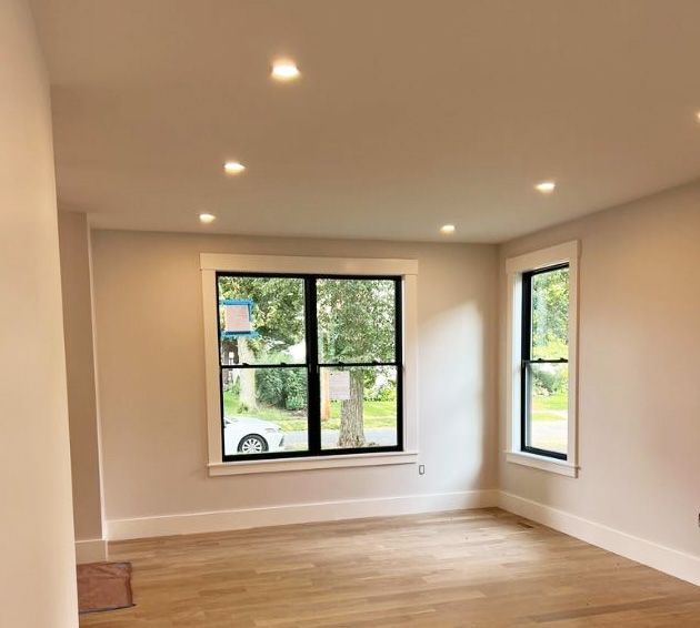 A room with light wood floors, beige walls, recessed ceiling lights, and windows with black frames and white trim.
