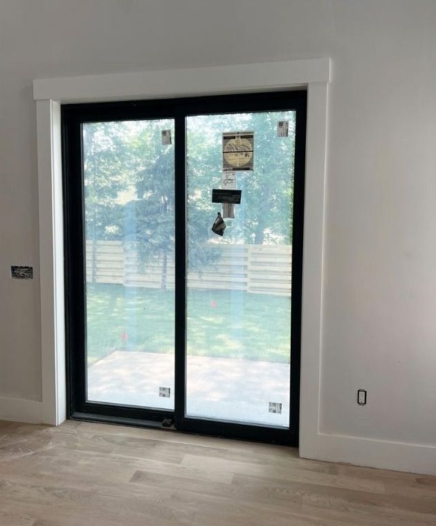 A black-framed sliding glass door with white trim, installed in a room with light-colored walls and wood flooring.