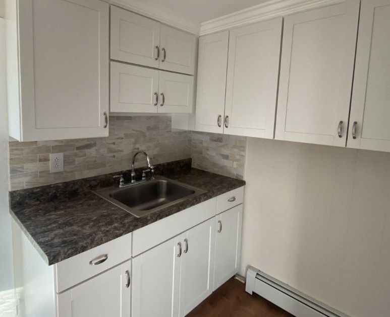 White kitchen cabinets with silver hardware and a dark speckled countertop featuring a single stainless steel sink.