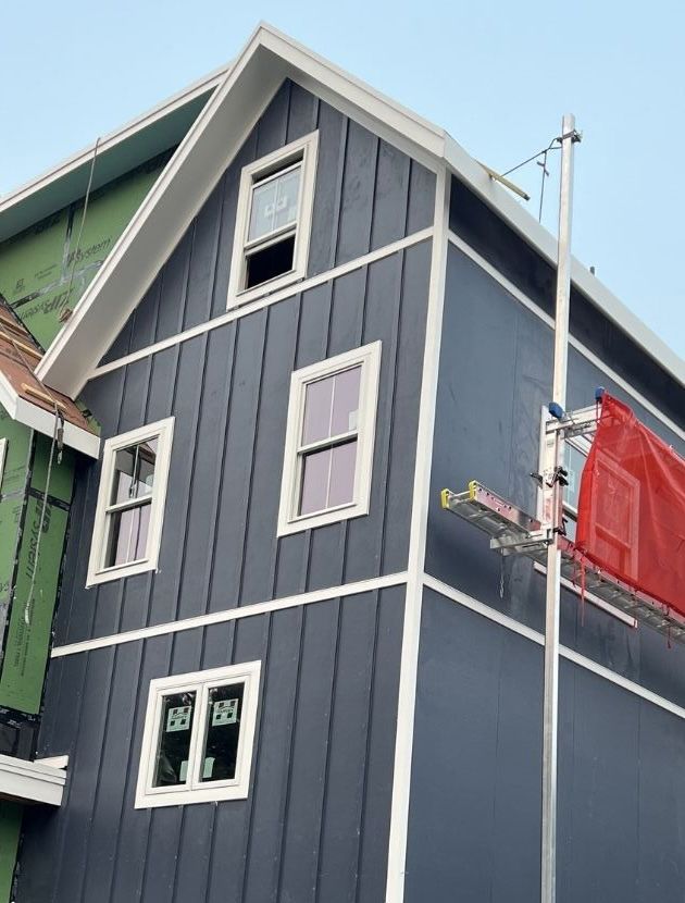 A dark blue, two-story house with board-and-batten siding and white trim under construction.