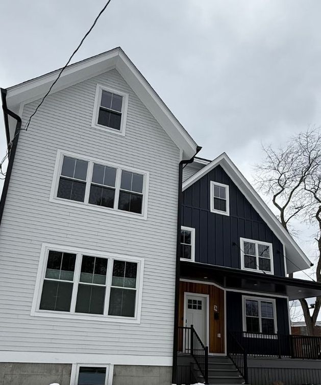 A modern two-story home with light gray horizontal siding and dark blue vertical siding under a cloudy sky.