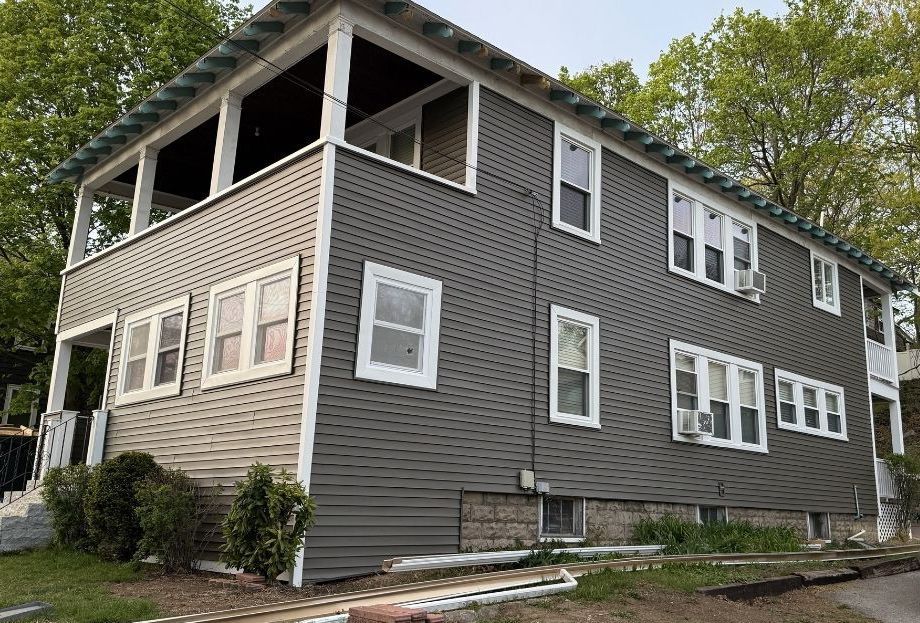 A two-story house with dark gray horizontal siding, white trim, and an open-air porch on the upper left corner.