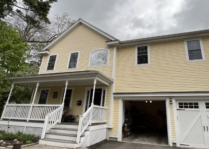 A pale yellow two-story house with white trim, featuring a covered front porch and an attached two-car garage.