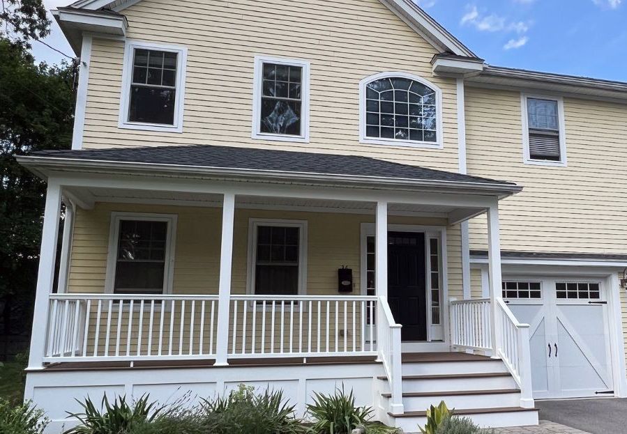 A yellow two-story house with a covered front porch, white trim, and an attached garage under a blue sky.