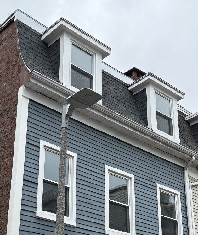 A modern streetlight stands in front of a blue-sided building with two dormer windows on a mansard roof.