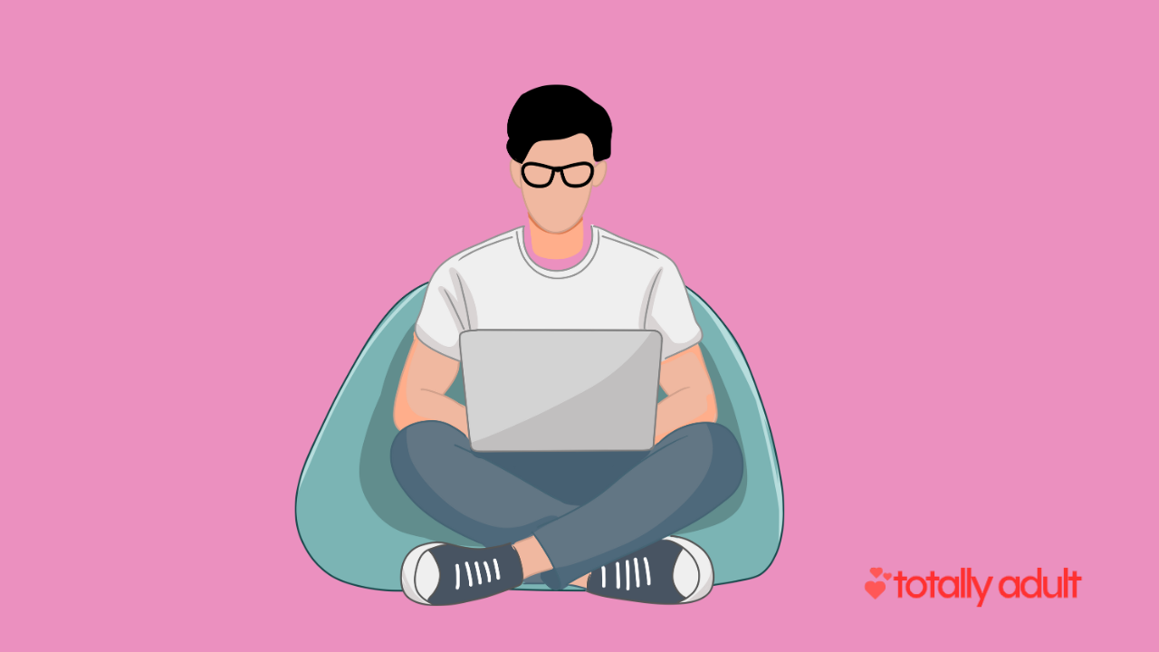 Person with glasses sitting on a bean bag chair, using a laptop, on a pink background.