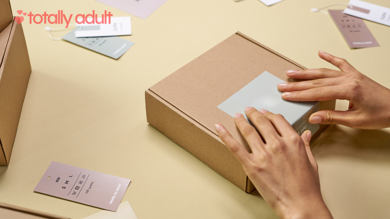 Hands carefully placing a label on a brown cardboard box, ready for shipping from an adult toy store.