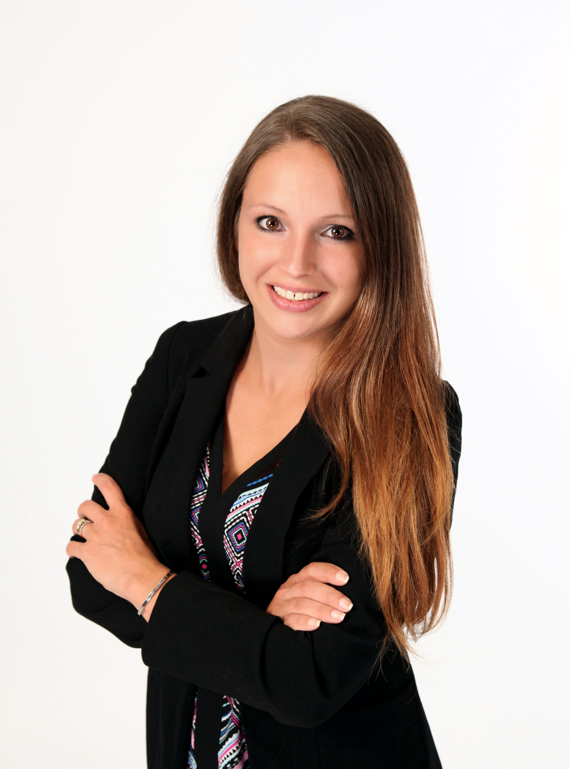 A woman in a black jacket is standing with her arms crossed and smiling.