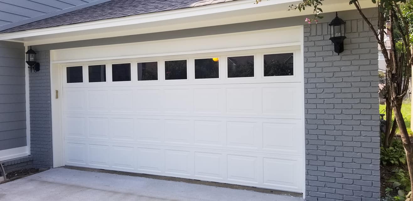A white garage door is on the side of a brick house.