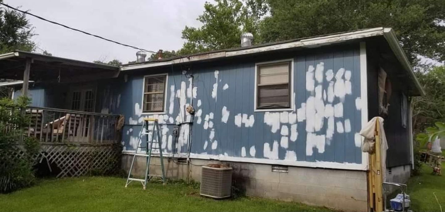A blue house with white trim is sitting on top of a lush green field.