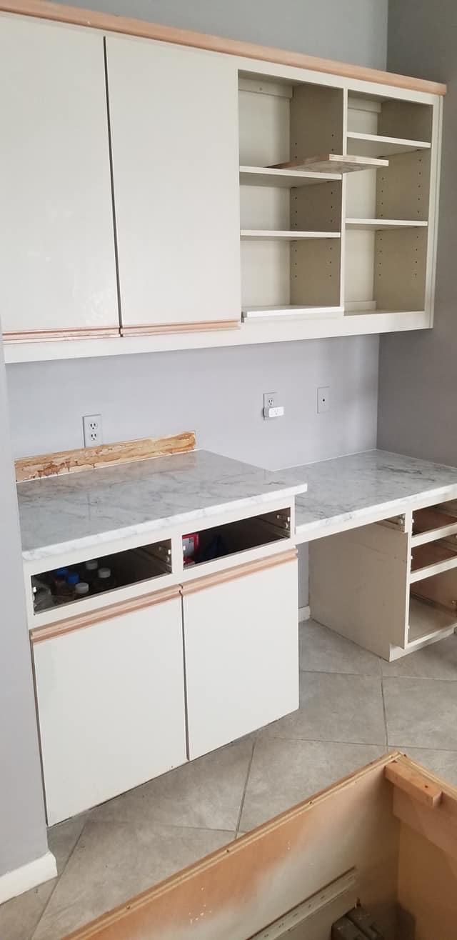 A kitchen with white cabinets and shelves and a desk.