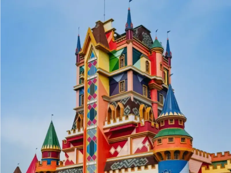 Castelo colorido de vários andares com diversas torres e um céu azul ao fundo.