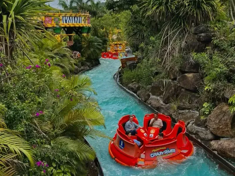 Passeio de jangada em um parque de diversões: barcos vermelhos em um rio turquesa cercado por vegetação.