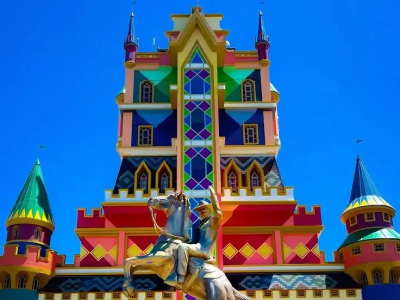 Castelo colorido com uma estátua de um cavaleiro a cavalo na frente, sob um céu azul brilhante.