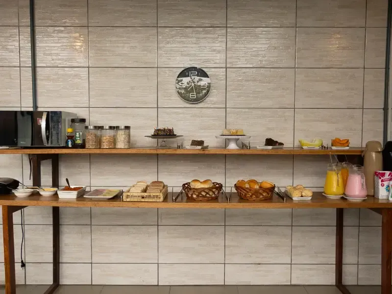 Buffet de café da manhã com doces, pães, sucos e condimentos em prateleiras de madeira.