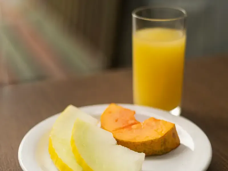 Um prato com fatias de melão e um copo de suco de laranja.