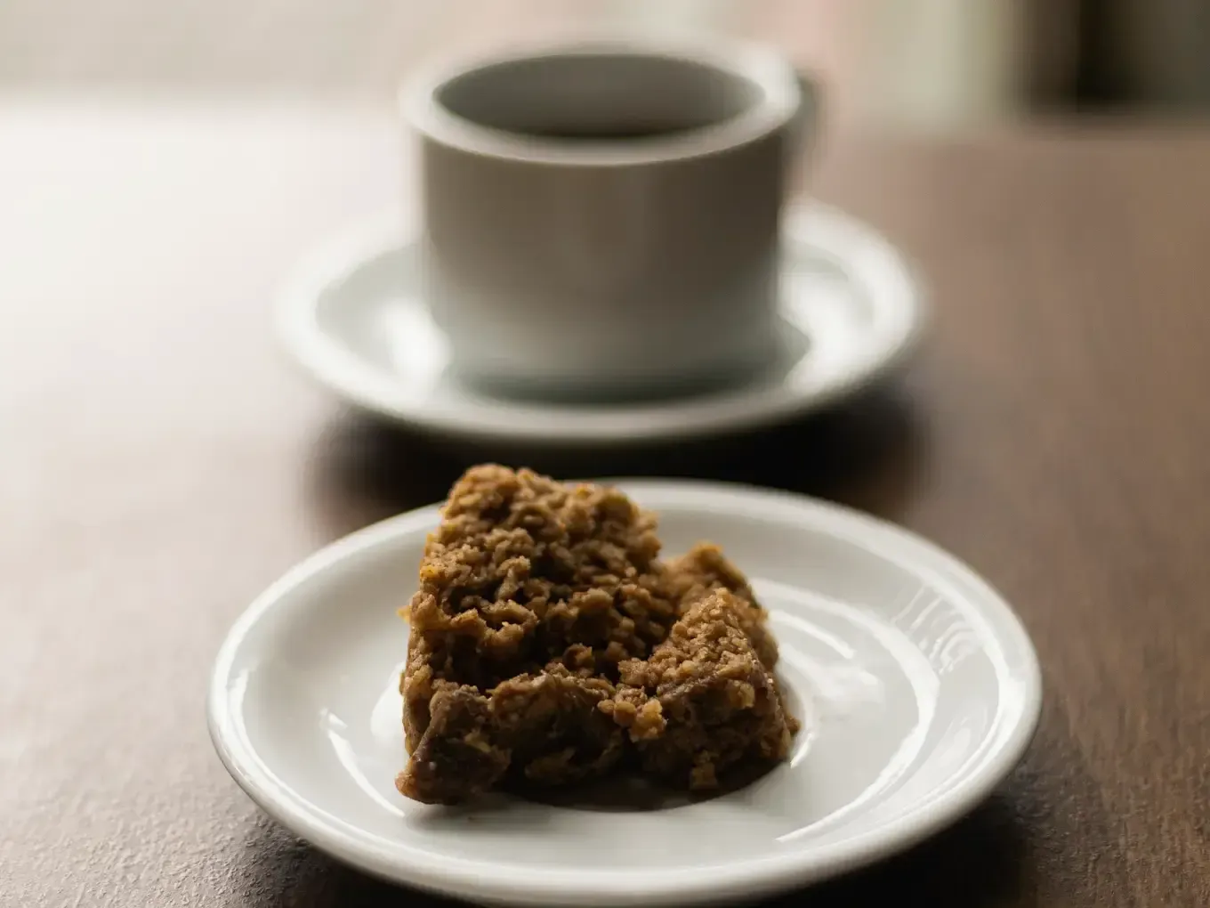 Café e um bolo de migalhas em pratos brancos, sobre uma mesa marrom.