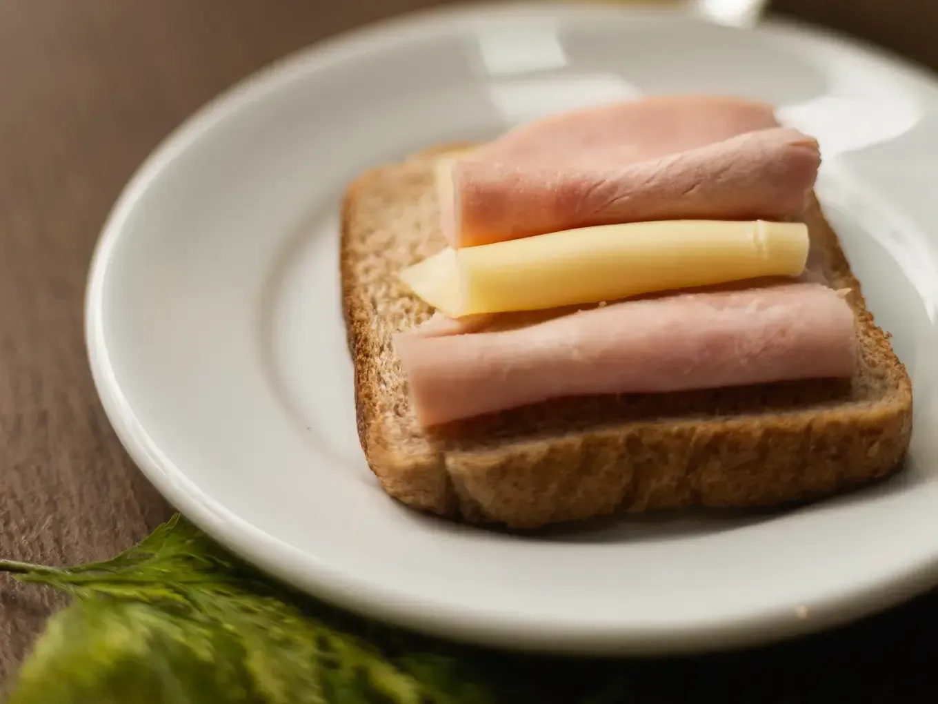 Sanduíche de presunto e queijo em pão integral, empilhado em um prato branco.
