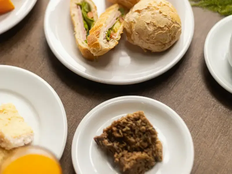 Pratos de comida sobre uma mesa, incluindo sanduíches, pão e um brownie.