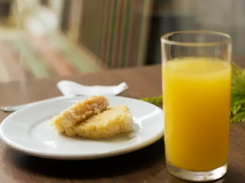 Prato com comida frita e copo de suco de laranja sobre uma mesa de madeira.